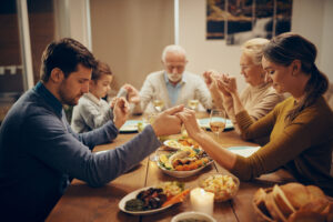 multi generation family holding hands and praying during lunch i